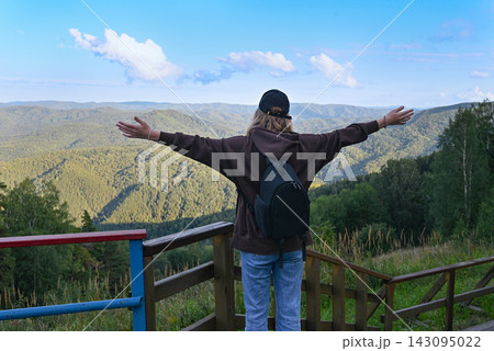 Young energetic girl with backpack having fun on edge of cliff in mountains at sunset against background of clouds. 143095022