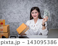Startup SME freelance woman holding lot of US dollars money and packing box proud smile working at home office. Online marketing packing box delivery, online sales. 143095386
