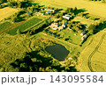 Aerial view of rural village with green fields, farmhouses, and small pond under golden hour  143095584