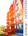 Modern apartment building with bold orange and blue facade, balconies, and warm sunlight  143095589