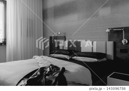 Monochrome Italian bedroom with leather biker jacket on upholstered bed 143096786