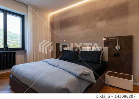 Contemporary primary bedroom with upholstered bed and warm indirect lighting 143096807