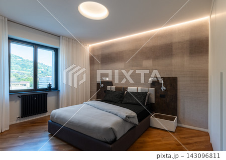 Contemporary Italian bedroom with upholstered bed and warm LED lighting 143096811