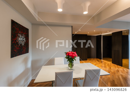 White dining table and floral bouquet beside a dark paneled entrance hall 143096826