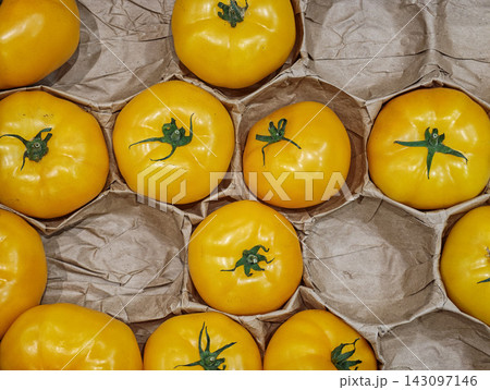 Fresh Yellow Tomatoes Arranged in Cardboard Produce Tray - illustrating fresh produce, grocery packaging, harvest and plastic-free food packaging concepts. Fresh Yellow Tomatoes Arranged in Cardboard Produce Tray - illustrating fresh produce, grocery packaging, harvest and plastic-free food packaging concepts. 143097146