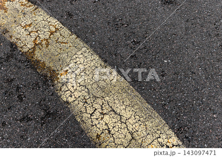 Close-up of a weathered yellow road line curving across cracked asphalt Close-up of a weathered yellow road line curving across cracked asphalt 143097471