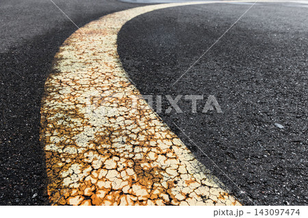 Close-up of a curved, cracked yellow road line on rough asphalt Close-up of a curved, cracked yellow road line on rough asphalt 143097474
