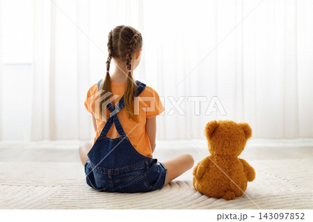 Preteen girl with braids sitting alone at home beside teddy bear Preteen girl with braids sitting alone at home beside teddy bear 143097852