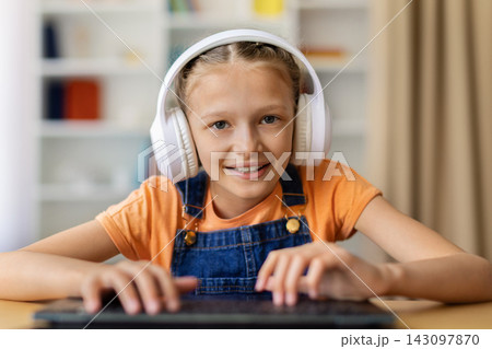 Sreteen girl in headphones looking at camera with hands on laptop keyboard Sreteen girl in headphones looking at camera with hands on laptop keyboard 143097870