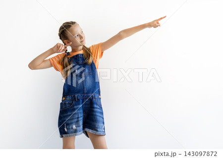 Teen girl in overalls pointing toward empty copy space against white background Teen girl in overalls pointing toward empty copy space against white background 143097872