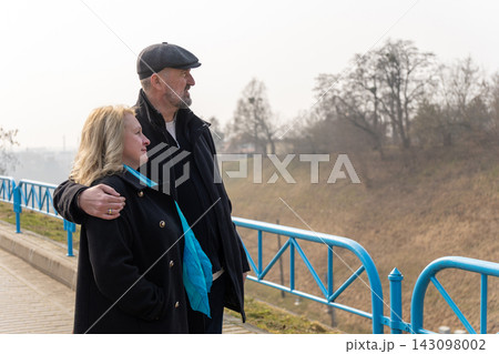 A mature couple embrace beside a blue railing outdoors. A mature couple embrace beside a blue railing outdoors. 143098002