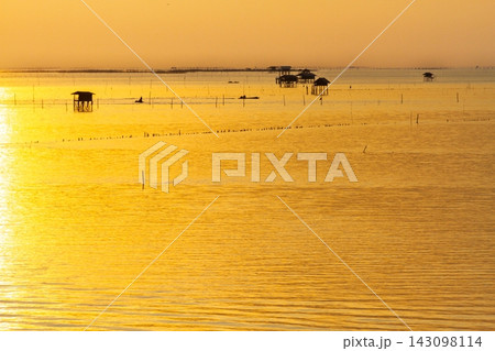 Golden sunset over the calm sea with traditional stilt houses and small fishing boats at dusk Golden sunset over the calm sea with traditional stilt houses and small fishing boats at dusk 143098114