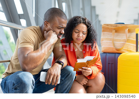 Concerned young Black couple sitting beside luggage at airport while checking passports 143098540