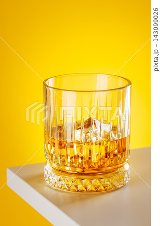 Whiskey glass with ice on yellow background minimal drink still life Whiskey glass with ice on yellow background minimal drink still life 143099026