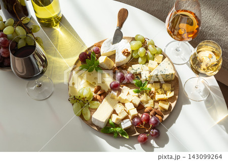 Assortment of delicious cheeses with grapes and wine presented on wooden board with glasses Assortment of delicious cheeses with grapes and wine presented on wooden board with glasses 143099264