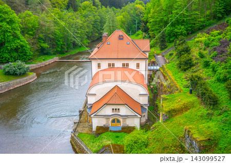 Small hydroelectric power plant is situated along the Labe River. It is surrounded by trees and hills. Water flows next to the plant and reflects the greenery in the area. Small hydroelectric power plant is situated along the Labe River. It is surrounded by trees and hills. Water flows next to the plant and reflects the greenery in the area. 143099527