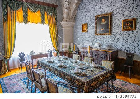 The dining area of Cervena Lhota Castle shows a large table set for a meal. The room has detailed walls, large windows, and several decorations contributing to its historic look. 143099733