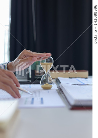 Close up of businessman analyzing growth charts and marketing statistics in office with hourglass on desk. Time management and financial analysis concept. Close up of businessman analyzing growth charts and marketing statistics in office with hourglass on desk. Time management and financial analysis concept. 143099996
