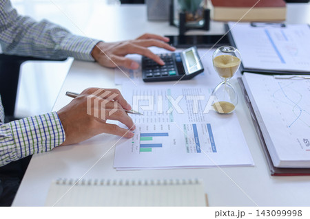 Businessman, accounting, banker working analyzing data with hourglass on desk. Concept for time management and financial analysis. Businessman, accounting, banker working analyzing data with hourglass on desk. Concept for time management and financial analysis. 143099998