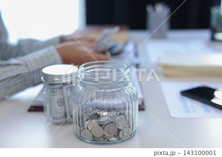 Close up glass jars filled with money and coins with businessman counting money in background. 143100001
