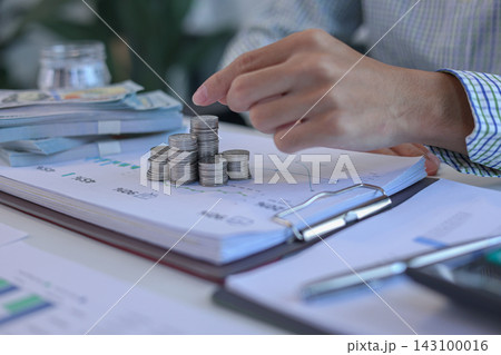 Businessman placing coin on top of coinstacks while engaging in financial planning or investment tracking on office desk 143100016