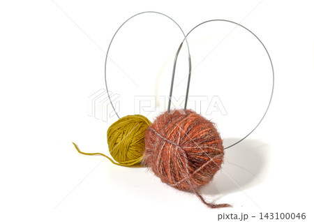 Knitting still life with orange and yellow yarn balls, circular needles, and sewing accessories on white 143100046