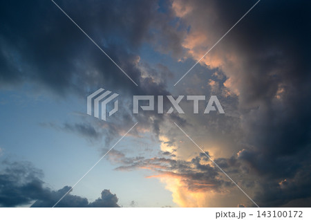 Dramatic sunset skyscape featuring dark storm clouds and warm golden illumination Dramatic sunset skyscape featuring dark storm clouds and warm golden illumination 143100172