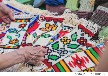 Traditional Woven Rugs with Folk Motifs at Kotel Market. Hands arrange colorful handmade woven rugs with floral, geometric and folk motifs at outdoor traditional craft market Traditional Woven Rugs with Folk Motifs at Kotel Market. Hands arrange colorful handmade woven rugs with floral, geometric and folk motifs at outdoor traditional craft market 143100597