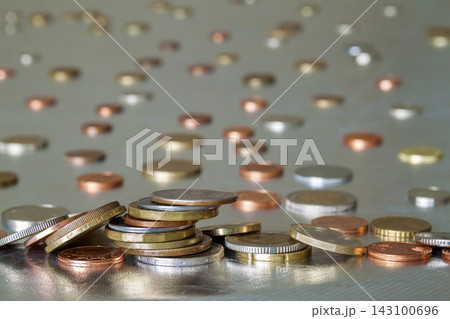 Pile of shiny coins different sizes and colors stacked unevenly on each other on colorful blurred blue abstract background. Money saving and financial risk concept. 143100696