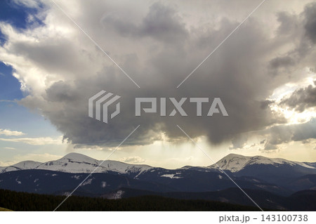 Fantastic view of huge white dark foreboding stormy cloud covering blue sky low over mountains Hoverla and Petros in Carpathian mountains range with bright snow on tops. Beauty and power of nature. Fantastic view of huge white dark foreboding stormy cloud covering blue sky low over mountains Hoverla and Petros in Carpathian mountains range with bright snow on tops. Beauty and power of nature. 143100738