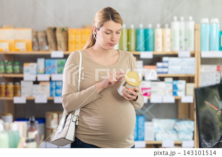In sales area of drug store, pregnant woman examines formula for feeding packaging 143101514