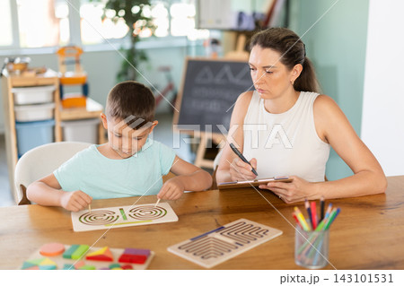 Child psychologist observing boy tracing labyrinths with both hands 143101531