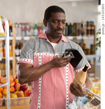 African man customer at shop scans QR code on wine bottle using phone camera African man customer at shop scans QR code on wine bottle using phone camera 143101805