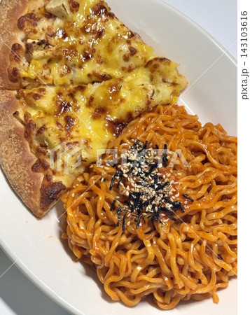 Spicy buldakmyeon noodles with vibrant red sauce served alongside a cheesy pizza, creating a bold combination of intense heat and savory, rich flavors in one satisfying meal 143103616