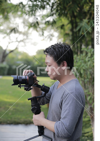 A man holds a camera stabilizer and checks the controls. He is setting up for smoother video recording. A man holds a camera stabilizer and checks the controls. He is setting up for smoother video recording. 143104048