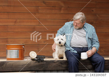 Terrace oil maintenance setup shows a homeowner, wooden deck, bucket, sanding tools, gloves, and dog during outdoor renovation. 143104307