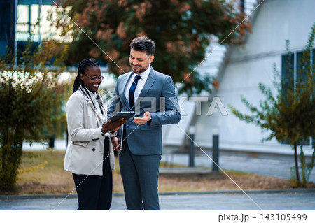 Diverse business people discussing digital tablet outdoors Diverse business people discussing digital tablet outdoors 143105499