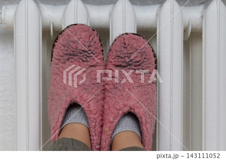 Feet in cozy pink slippers placed directly on top of a classic radiator to get warm Feet in cozy pink slippers placed directly on top of a classic radiator to get warm 143111052