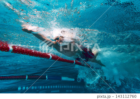 Competitive swimmer racing freestyle underwater in pool lane. 143112760