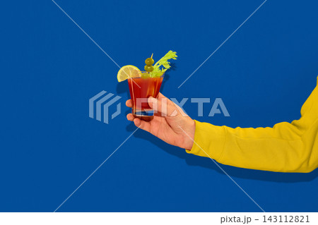 Hand holding bloody mary cocktail on blue background. 143112821