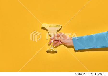 Hand holding margarita cocktail on yellow background. Hand holding margarita cocktail on yellow background. 143112825