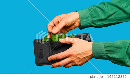 Hands filling black wallet with green leaves on blue background. Hands filling black wallet with green leaves on blue background. 143112883