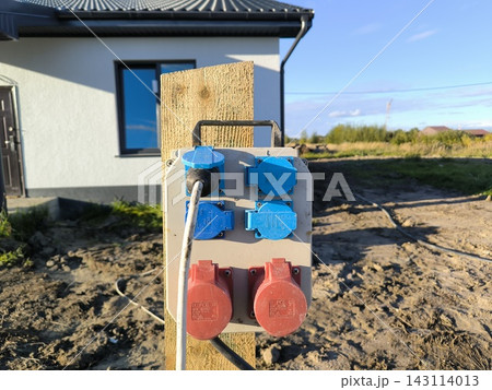 Power panel with sockets on a pole near a house under construction 143114013