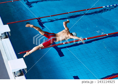 Overhead view of male swimmer diving into blue pool lane. Overhead view of male swimmer diving into blue pool lane. 143114925