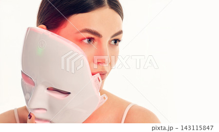 Woman holding LED light therapy face mask for advanced skincare treatment. Woman holding LED light therapy face mask for advanced skincare treatment. 143115847