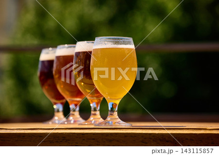 Foamy craft beer tasting flight on wooden terrace with green background. Foamy craft beer tasting flight on wooden terrace with green background. 143115857