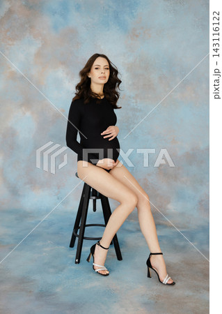 Pregnant model sitting on stool caressing her belly Pregnant model sitting on stool caressing her belly 143116122
