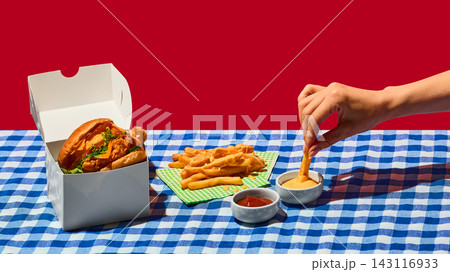Chicken burger with fries and dipping sauces on checkered picnic table. 143116933