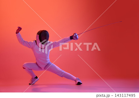 Female fencer holding powerful low guard position under vibrant red lighting. 143117495