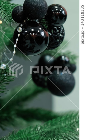 Elegant black shiny and matte baubles hanging on decorated Christmas tree branch closeup. Dark holiday ornaments with beads garland decoration for creative winter festive home interior. Vertical shot. 143118335